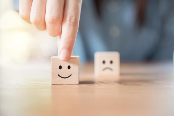 Close up hand choose smiley face and blurred sad face icon on wood cube