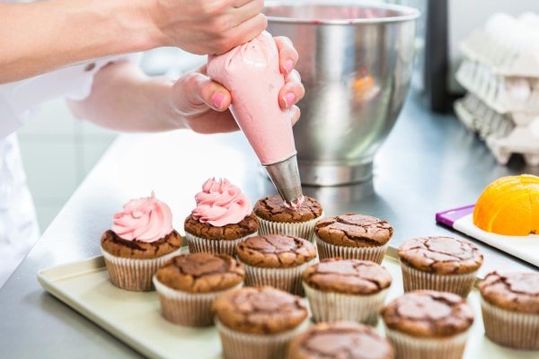 Women in pastry bakery as confectioner glazing muffins with icing bag