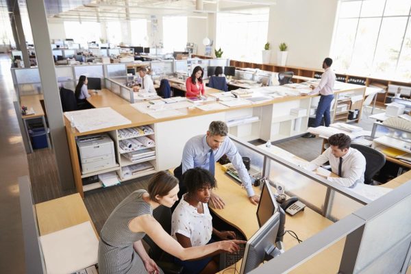 Colleagues working at a womanâ"u20acs workstation in a busy office